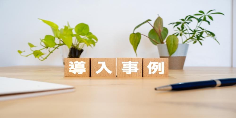 木製ブロックに「導入事例」と書かれた文字が並び、背景に観葉植物とペンが置かれたデスクが映る明るいイメージ写真