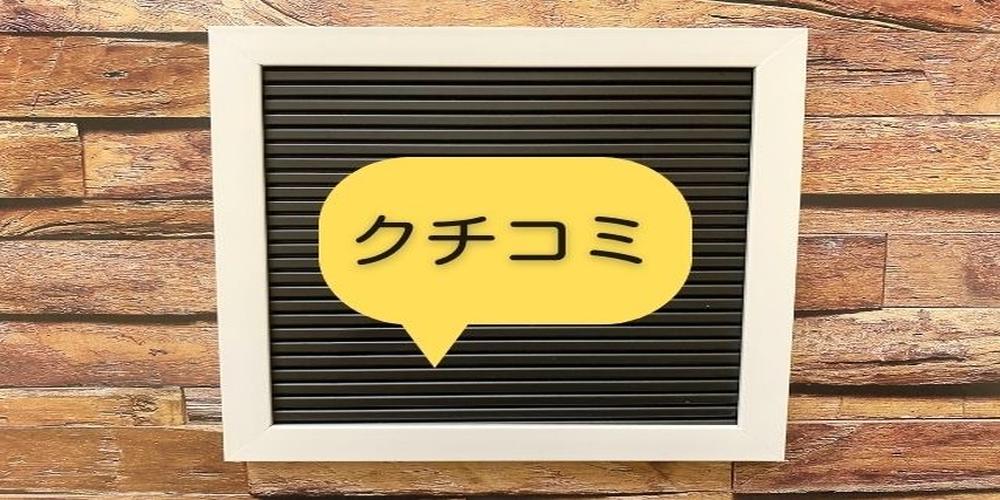「クチコミ」と書かれた黄色い吹き出しが黒いボードの中央に配置され、背景には木目調の壁が写っている画像