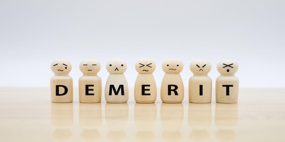 「DEMERIT」と書かれた木製ピースが並び、それぞれ異なるネガティブな表情をしているイメージ写真（デメリットや注意点を表現）