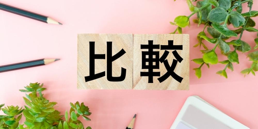 ピンクの背景に観葉植物と鉛筆、中央に「比較」と書かれた木製ブロック
