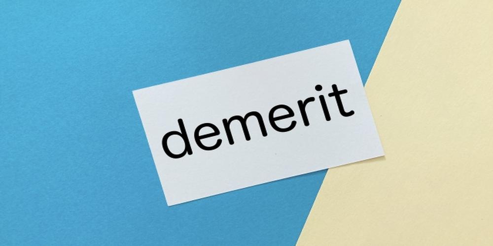 「demerit」と書かれた白いカードが青とクリーム色の背景の上に置かれている画像（デメリット・短所のイメージ）