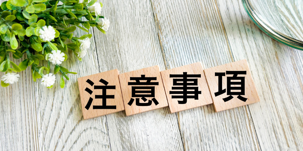 木製のブロック4つに黒文字で「注意事項」と並べ、左上に観葉植物、右上に虫眼鏡が置かれたデスク風景