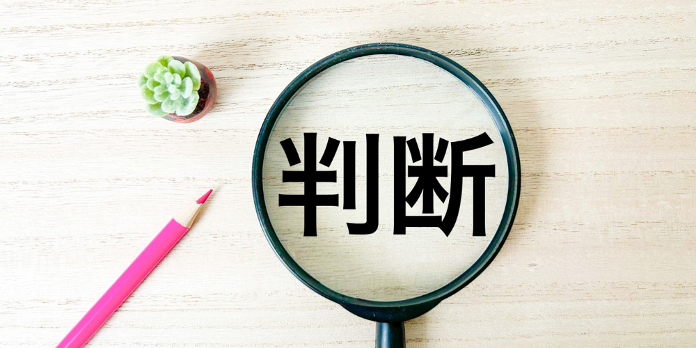 デスク上に置かれた虫眼鏡の中に黒文字で「判断」と書かれた付箋が拡大されている風景