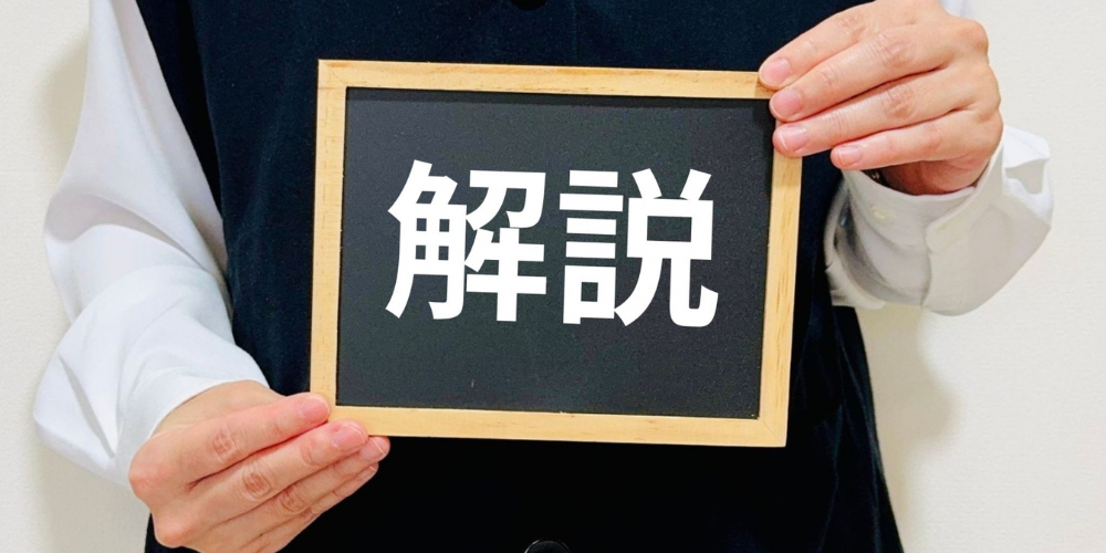 白いシャツと黒いベストを着た人物が、黒板フレームのプラカードに「解説」と大きく書かれた文字を掲げている様子のイメージ画像
