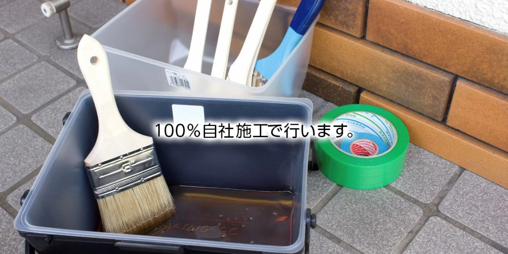この画像は、タイル張りの床の上に塗料トレイと刷毛、マスキングテープなどの塗装用道具が置かれ、中央に「100%自社施工で行います。」の文字が重ねられている様子が写っています。